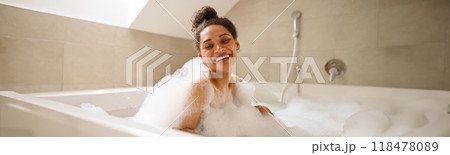 A happy woman is bathing in a foamfilled bathtub, smiling at the fixture 118478089