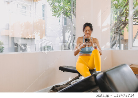 Lazy woman in Yellow Blue fitness outfit sitting and using mobile in the gym. 118478714