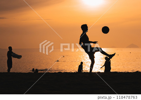 Silhouette of a man kicking a ball playing traditional Asian beach football on beach by the sea at sunset 118478763