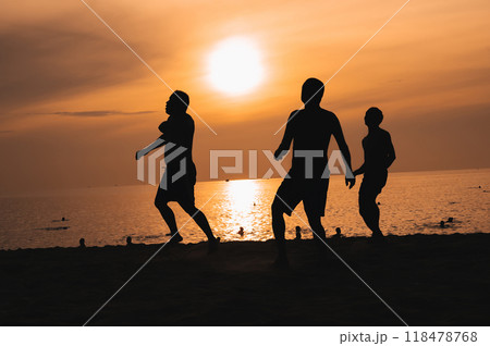 Silhouettes of Asian men playing beach soccer on beach by the sea at sunset 118478768