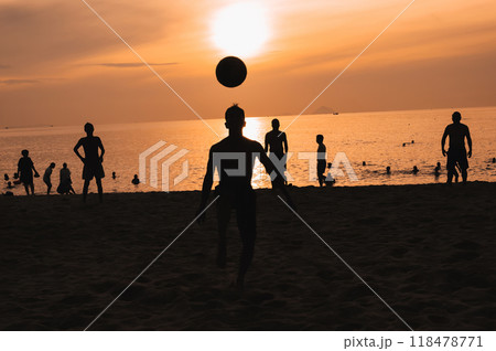 Silhouettes of a group of Asian men playing traditional beach soccer on a beach by sea at sunset 118478771
