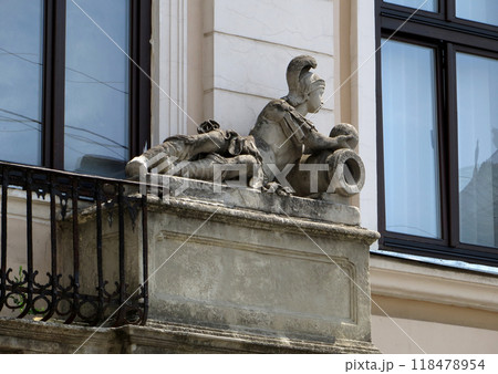 Reclining figure of a Roman soldier with cannon and a cannonball. Stone statue on the old building. Reclining figure of a Roman soldier with cannon and a cannonball. Stone statue on the old building. 118478954