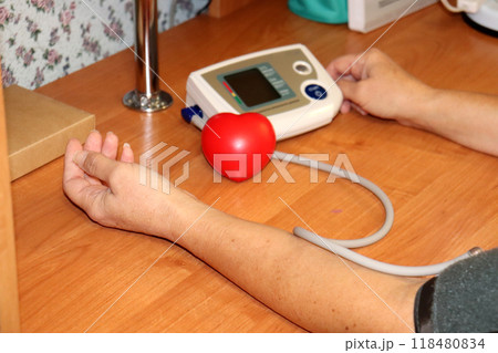 A woman measures blood pressure - electronic device and a red hand trainer A woman measures blood pressure - electronic device and a red hand trainer 118480834