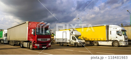 Colorful modern big semi-trucks and trailers of different makes and models stand in row on flat parking lot of truck stop in sunshine Colorful modern big semi-trucks and trailers of different makes and models stand in row on flat parking lot of truck stop in sunshine 118481983