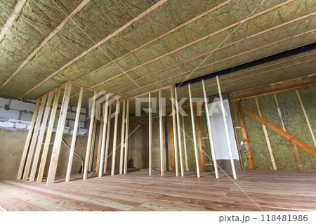 Construction and renovation of big spacious empty unfinished attic room with oak floor, walls and ceiling insulated with rock wool and fiber glass for cold barrier and wooden frame for future walls. Construction and renovation of big spacious empty unfinished attic room with oak floor, walls and ceiling insulated with rock wool and fiber glass for cold barrier and wooden frame for future walls. 118481986