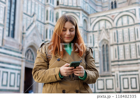 Woman walking on city street checks phone. 30s girl using smartphone near famous Duomo cathedral in Florence. Stylish women visiting Italian landmarks. Concept of travel, tourism and vacation in city Woman walking on city street checks phone. 30s girl using smartphone near famous Duomo cathedral in Florence. Stylish women visiting Italian landmarks. Concept of travel, tourism and vacation in city 118482335