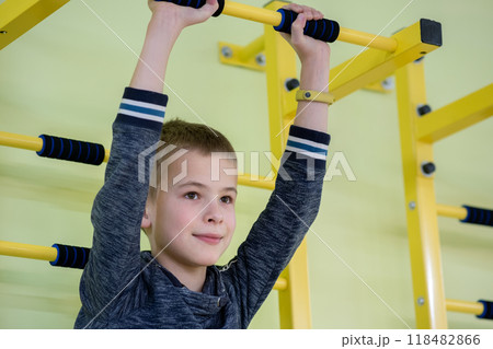 Young child boy exercising on a wall ladder bar inside sports gym room in a school. 118482866