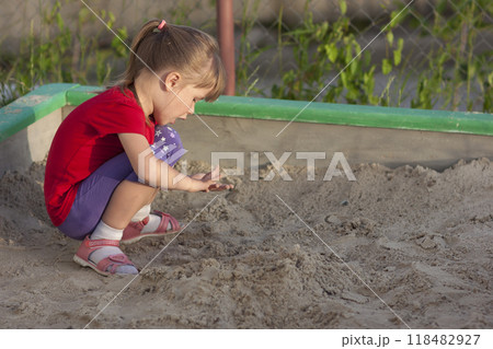 Little girl playing in sandbox on a sunny summer day Little girl playing in sandbox on a sunny summer day 118482927