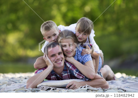 Family portrait of young happy mother, father and two cute blond children, boy and girl on bright summer day with green bokeh background. Happy family relations, love, care and perfect holiday concept 118482942