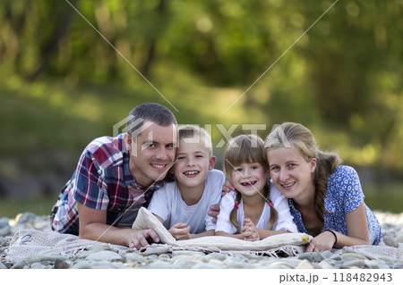 Family portrait of young happy mother, father and two cute blond children, boy and girl on bright summer day with green bokeh background. Happy family relations, love, care and perfect holiday concept 118482943