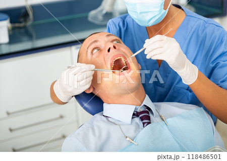 Qualified woman dentist in a protective mask treats a man patient 118486501