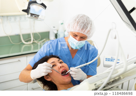 Focused man dentist in a protective mask treats a woman patient 118486698