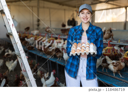 Smiling woman standing in henhouse with cardboard tray of eggs 118486719