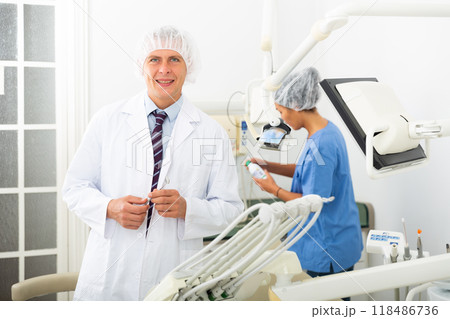Positive male dentist standing in dental office looking at camera 118486736