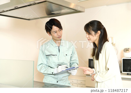 家庭のキッチンのIHコンロの前で会話する男性作業員と女性客 家庭のキッチンのIHコンロの前で会話する男性作業員と女性客 118487217