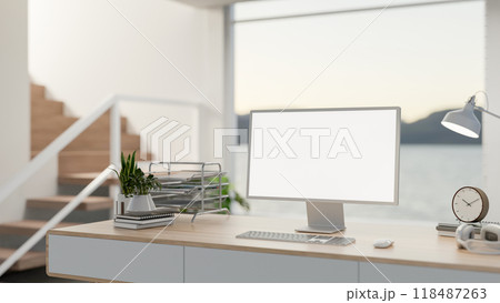 A computer desk in a contemporary home, featuring a large window behind it, with stairs nearby. A computer desk in a contemporary home, featuring a large window behind it, with stairs nearby. 118487263
