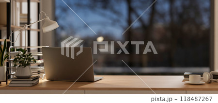 A rear view of a laptop on a wooden table, with a window showing an outdoor view at dusk. A rear view of a laptop on a wooden table, with a window showing an outdoor view at dusk. 118487267