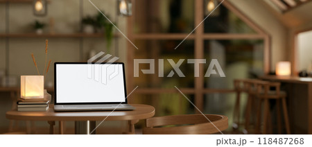 A laptop mockup sits on a wooden table in a cozy Scandinavian coffee shop at night. 118487268