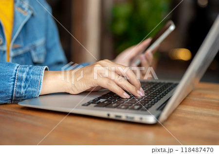 A close-up of a woman working on her laptop in a coffee shop, typing on the laptop keyboard. A close-up of a woman working on her laptop in a coffee shop, typing on the laptop keyboard. 118487470