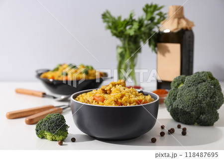 Pilaf in bowls, spices, vegetables and bottle on white background, close up 118487695