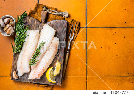 Raw cod fish fillets, codfish with rosemary on wooden board. Orange background. Top view. Copy space Raw cod fish fillets, codfish with rosemary on wooden board. Orange background. Top view. Copy space 118487775