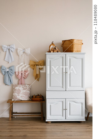 White dresser with bows hanging on the wall and straw basket on top in cozy and welcoming atmosphere children room White dresser with bows hanging on the wall and straw basket on top in cozy and welcoming atmosphere children room 118489080