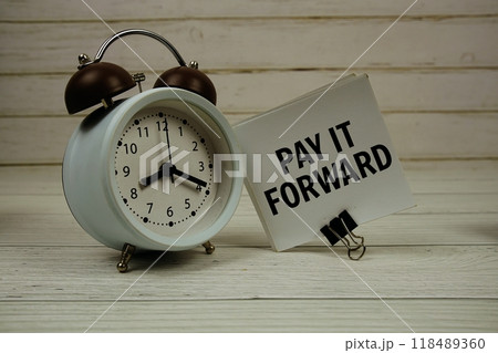 Pay It Forward text message on sticky note with alarm clcok on wooden background 118489360