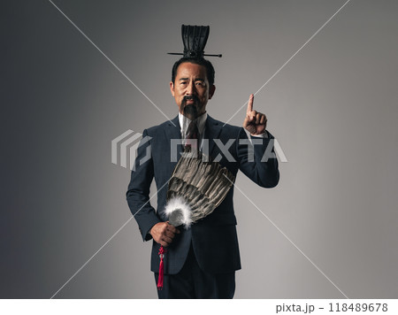 三国志に登場する諸葛孔明のような中国歴史上の軍師がビジネススーツを着て説明するシーン 118489678