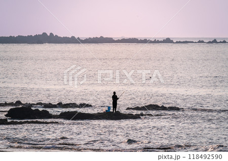 Solitude at Sunset: Fisherman on Rocky Shore. 118492590