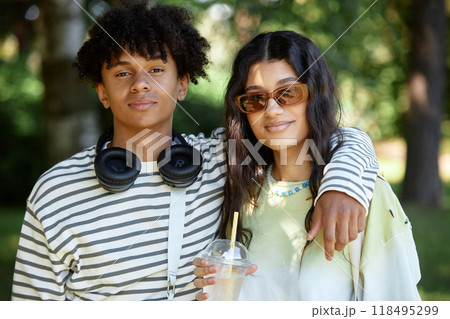 Portrait of African American teenage boy with headphones posing next to Middle Eastern girlfriend smiling for camera. Young couple enjoying summer day in park 118495299