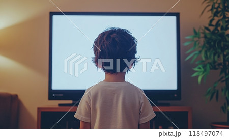 Young boy standing in front of TV with blank screen, dimly lit room. 118497074