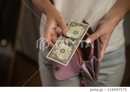 Woman putting one dollar bill in pink wallet 118497575