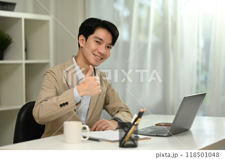 Professional businessman sitting at office desk and showing a thumbs up gesture Professional businessman sitting at office desk and showing a thumbs up gesture 118501048