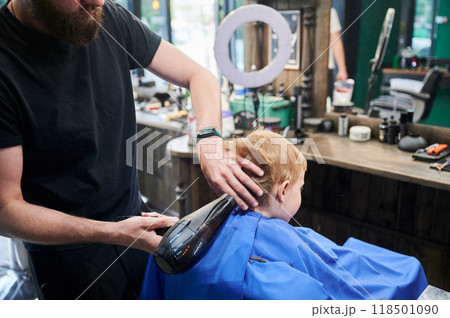 Back view of professional barber styling little boy's hair. Male hairdresser drying hair. Cute boy excited about his new hair style. Back view of professional barber styling little boy's hair. Male hairdresser drying hair. Cute boy excited about his new hair style. 118501090