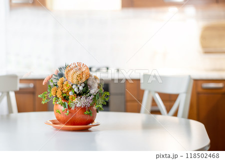 Thanksgiving day table setting decoration creative bouquet centerpieces with orange flowers in pumpkin as vase in modern home kitchen interior. Close up. Thanksgiving day table setting decoration creative bouquet centerpieces with orange flowers in pumpkin as vase in modern home kitchen interior. Close up. 118502468