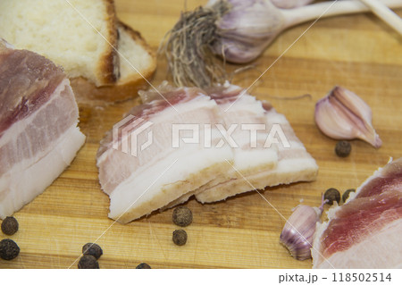 Ukrainian products raw lard with peppercorn and garlic, knife, slices of bread, salo lying on wooden board. Ukrainian traditional food concept. Ukrainian products raw lard with peppercorn and garlic, knife, slices of bread, salo lying on wooden board. Ukrainian traditional food concept. 118502514