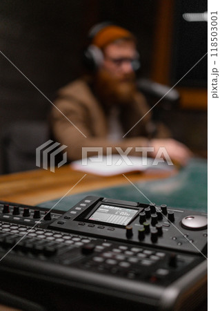 A podcaster is in a studio with recording equipment and microphones, ready to create content 118503001