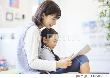 保育園で園児を膝に抱いて絵本を読む女性保育士 118503027