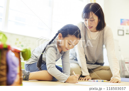 お絵描きをする園児に声をかける女性保育士 お絵描きをする園児に声をかける女性保育士 118503037