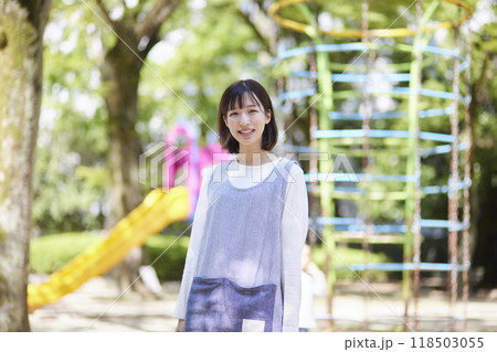 園庭の遊具を背景に立つ笑顔の女性保育士 118503055