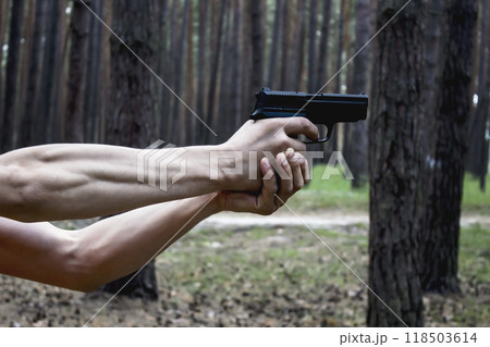 Strong Men's hands hold a gun against  forest background. Danger situation in the forest 118503614