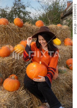 Woman holding a pumpkin sitting on hay bales Woman holding a pumpkin sitting on hay bales 118504372