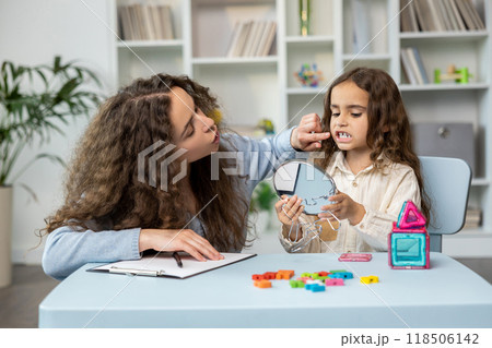 Cute long-haired girl exercising with a mirror at the speech therapist office Cute long-haired girl exercising with a mirror at the speech therapist office 118506142