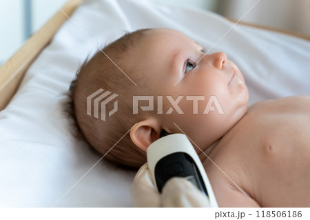 Female pediatrician with digital infrared thermometer measuring baby girl patient's ear temperature 118506186