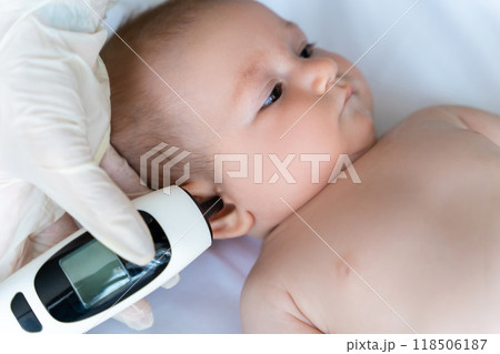 Female pediatrician with digital infrared thermometer measuring baby girl patient's ear temperature 118506187