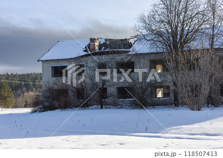 Abandoned building in a winter landscape, bathed in sunlight on snowy ground. Roof caved in, windows broken, telling a story of ruin and decay. Lonely and spooky, a reminder of the past. 118507413
