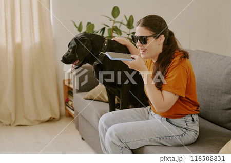 Happy woman with disability petting her black Labrador while speaking on smartphone 118508831