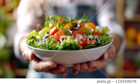 Fresh garden salad served in a bowl held by a person in a kitchen filled with vibrant vegetables during the afternoon 118509076