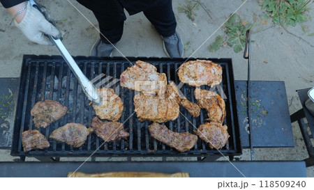 Barbecue outdoors. Grilling a raw meat steak on a burning fire, a man uses tongs to flip a grilled steak on a barbecue grill. Close-up of a delicious grilled meat steak. Barbecue outdoors. Grilling a raw meat steak on a burning fire, a man uses tongs to flip a grilled steak on a barbecue grill. Close-up of a delicious grilled meat steak. 118509240