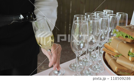 A woman pours champagne into a glass, close-up. Catering with sandwiches. 118509286